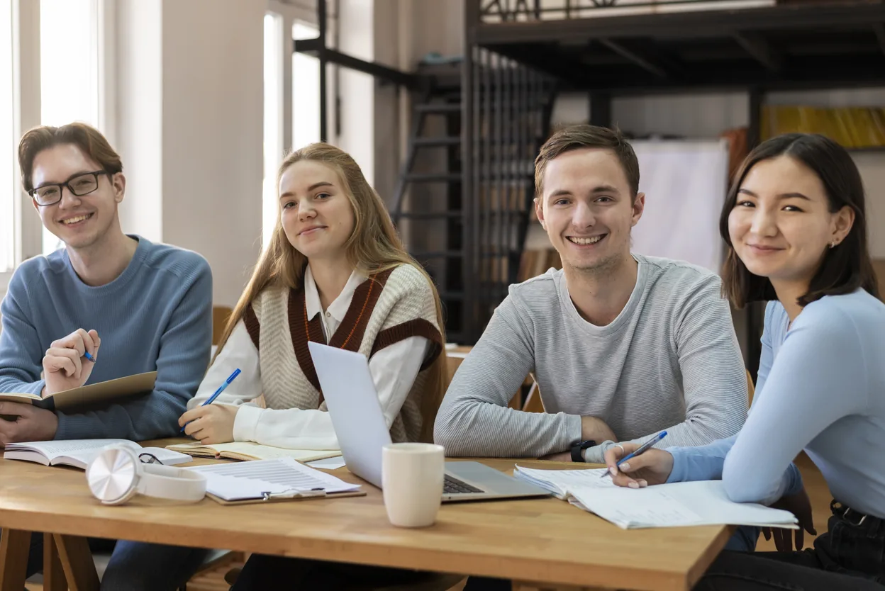 Four students smiling to camera around a shared study table